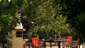 An outdoor patio with tables and chairs, surrounded by dense foliage. - Erifili Apartments (Corfu)