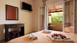A bedroom with a bed, a desk, a TV, and a sliding glass door to a balcony. - Erifili Apartments (Corfu)