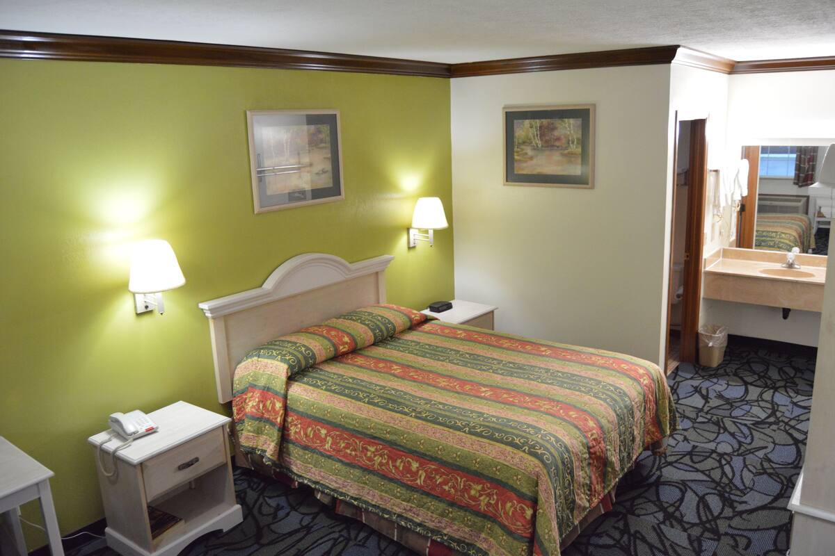 A hotel room with a bed, bedside tables, lamps, and a mirror.