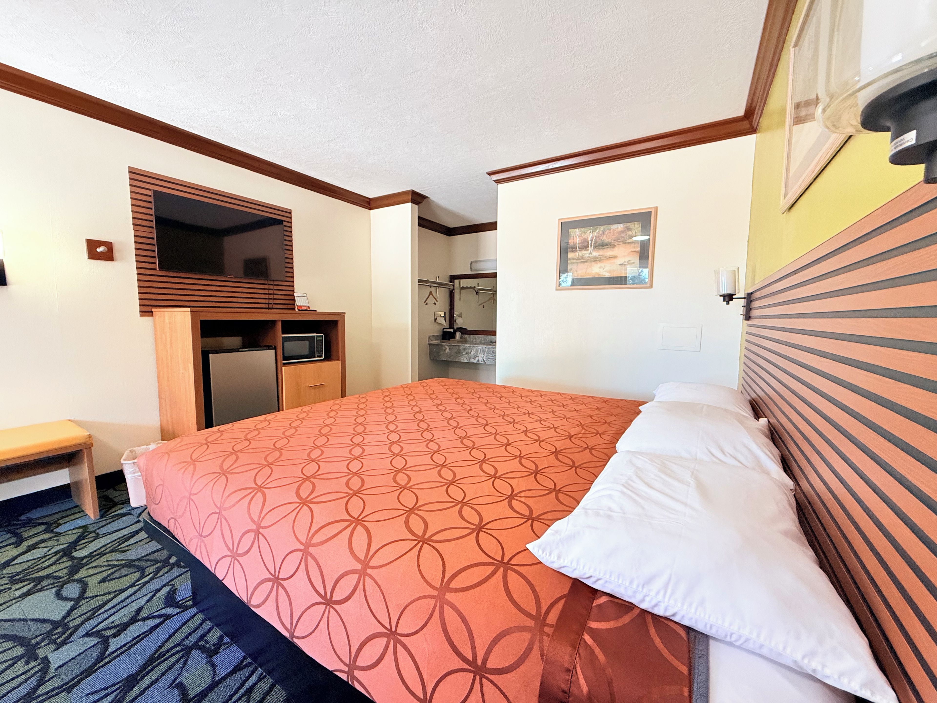 Een hotelkamer met een bed, een bureau, een spiegel, een kleine badkamer en een foto aan de muur.