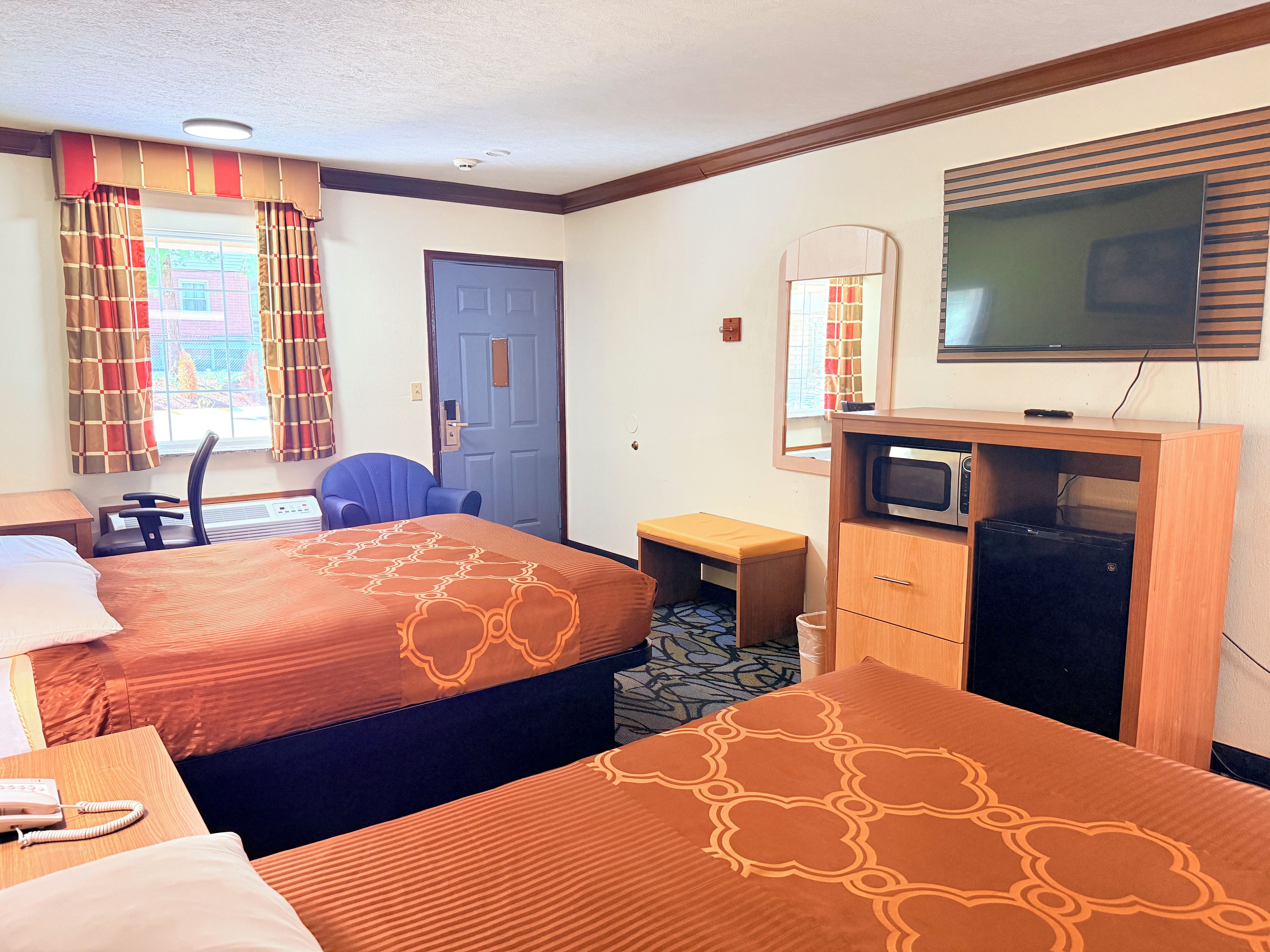 A hotel room with two beds, a desk, a chair, a television, and a microwave.