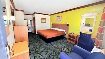 A hotel room with a bed, a desk, a chair, a mirror, and a carpeted floor.