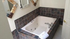 Une salle de bain dotée d’une grande baignoire, de murs recouverts de carreaux foncés et de trois miroirs décoratifs aux cadres originaux.