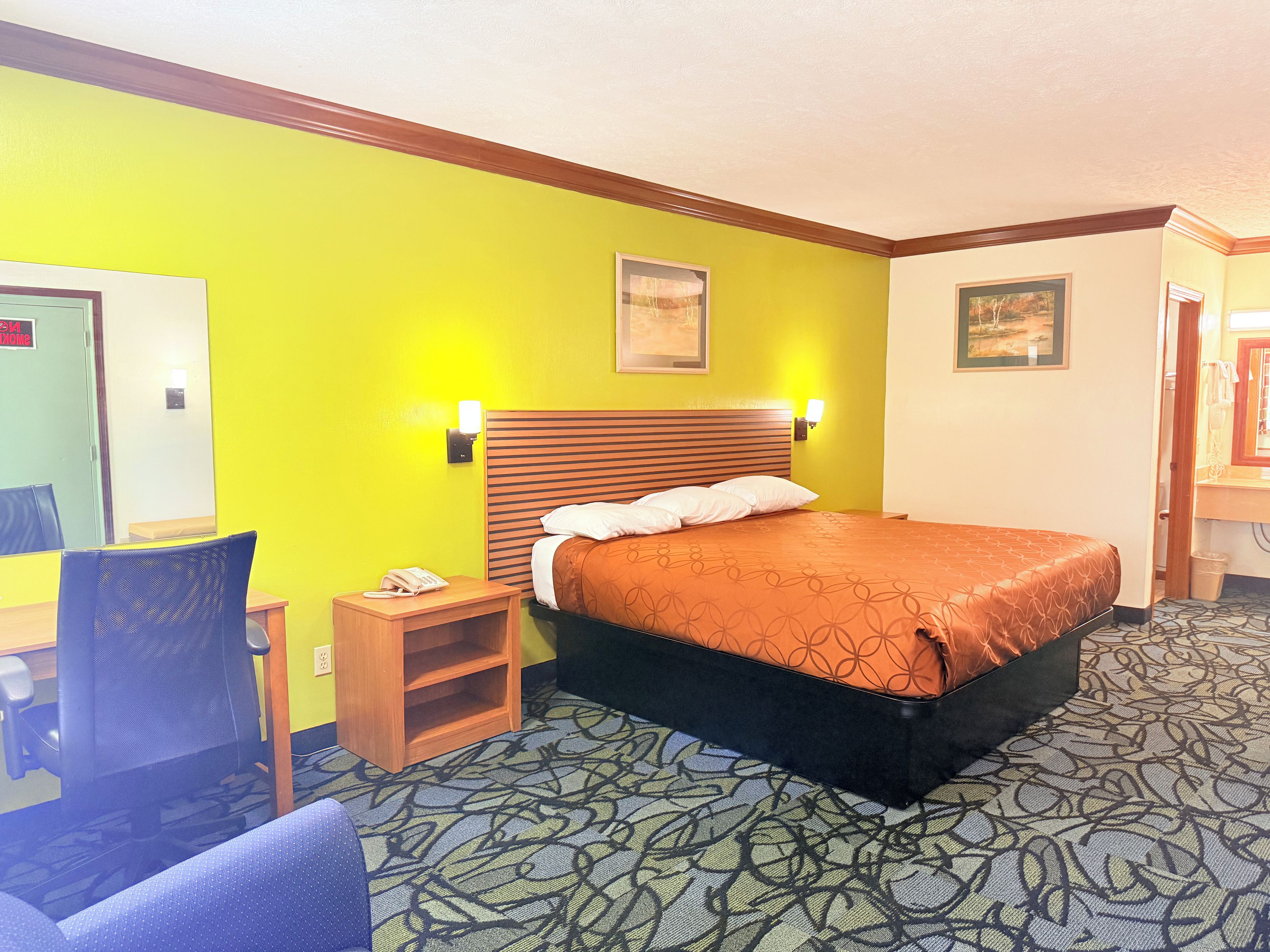 A hotel room with a bed, a chair, a nightstand, and a mirror.