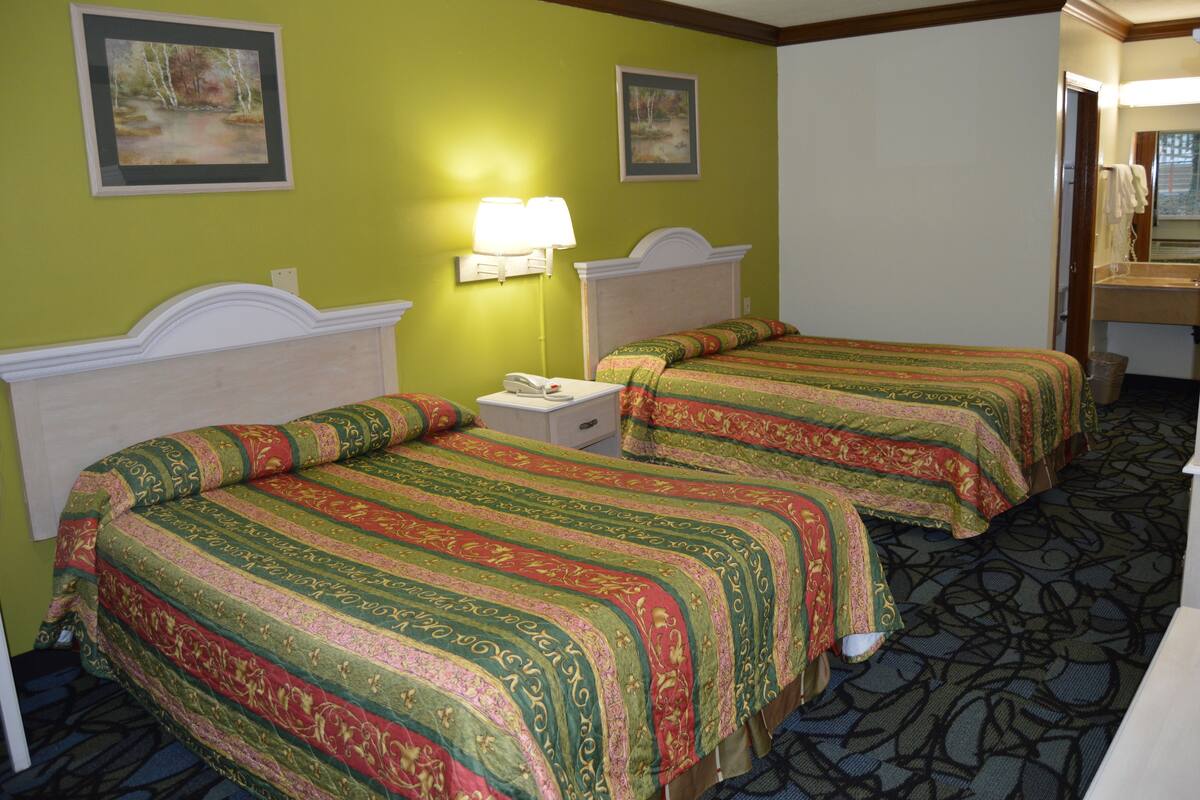 A hotel room with two beds, a nightstand, a lamp, and a bathroom visible through an open door.