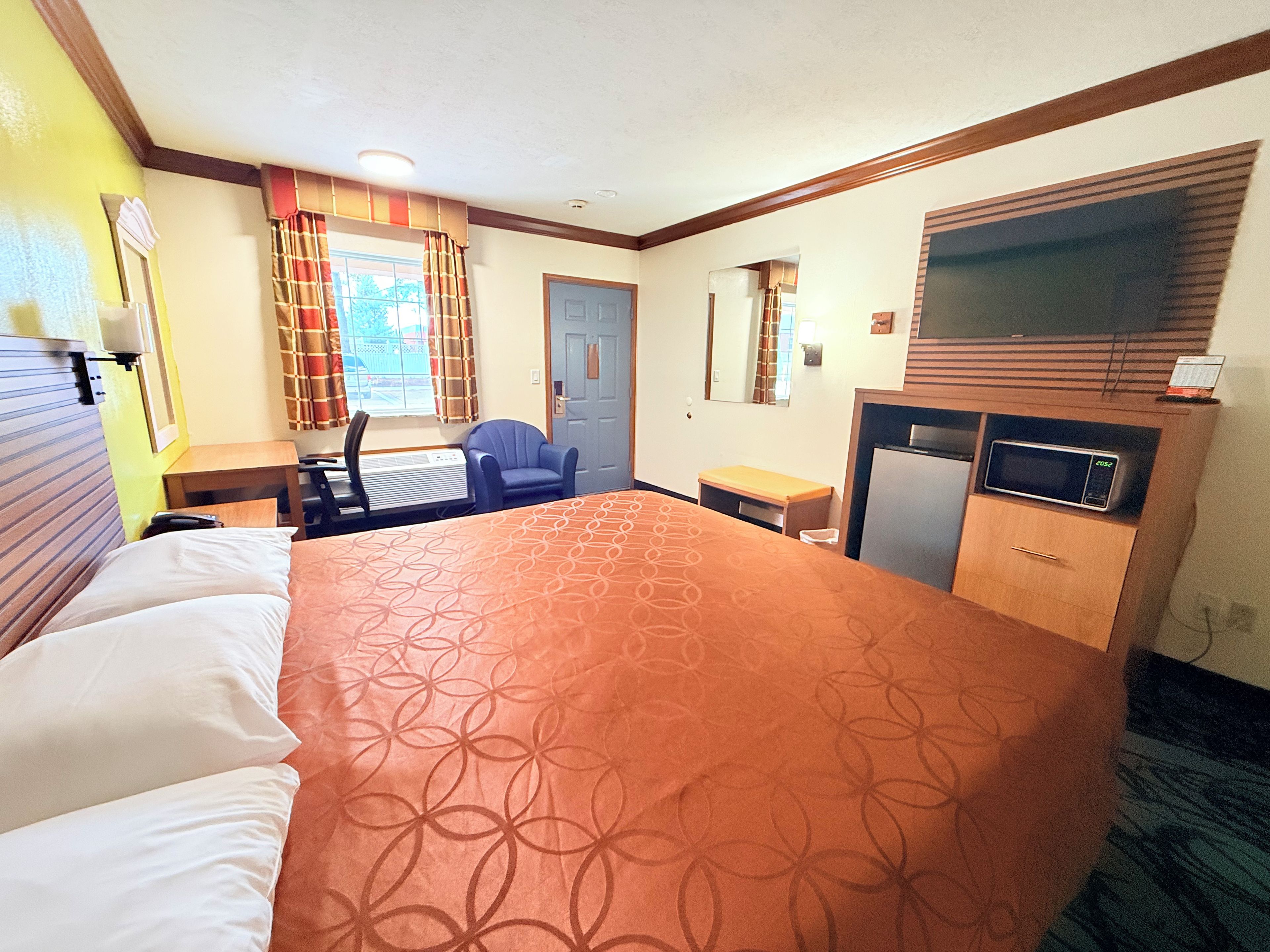 A hotel room with a large bed, a desk with a chair, a microwave, and a television.