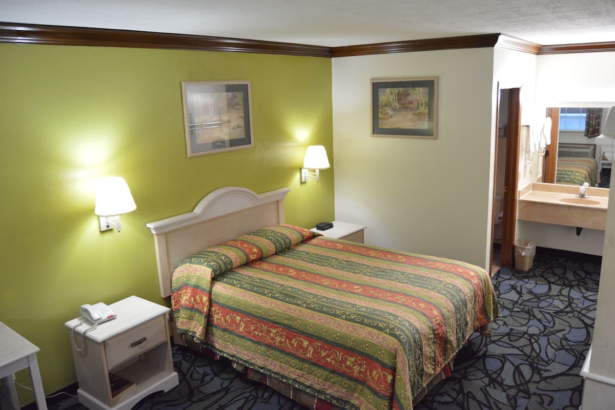 A hotel room with a bed, bedside tables, a lamp, a mirror, and a painting on the wall.