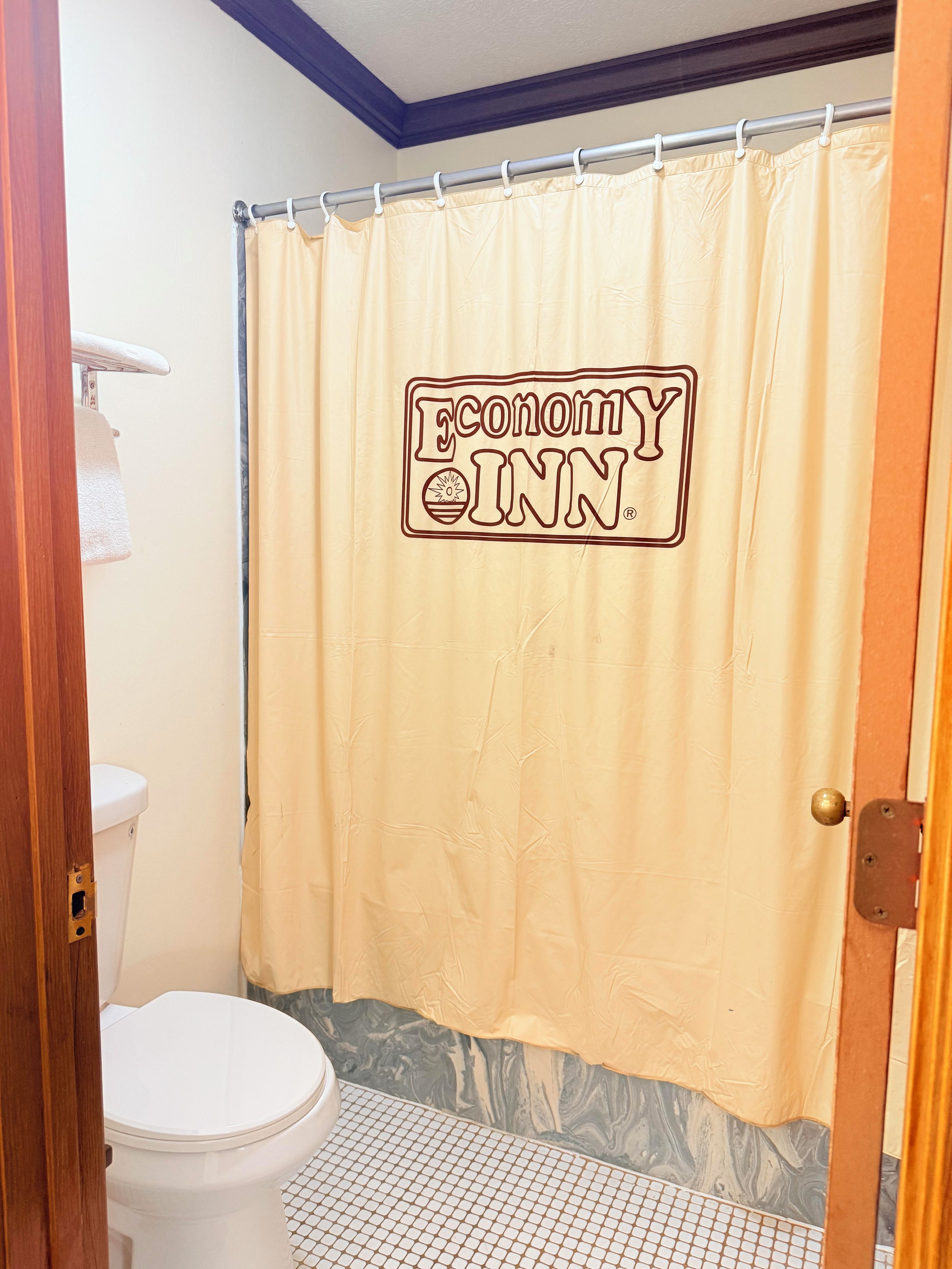 A bathroom with a shower curtain featuring a logo, a toilet, and a tiled floor.
