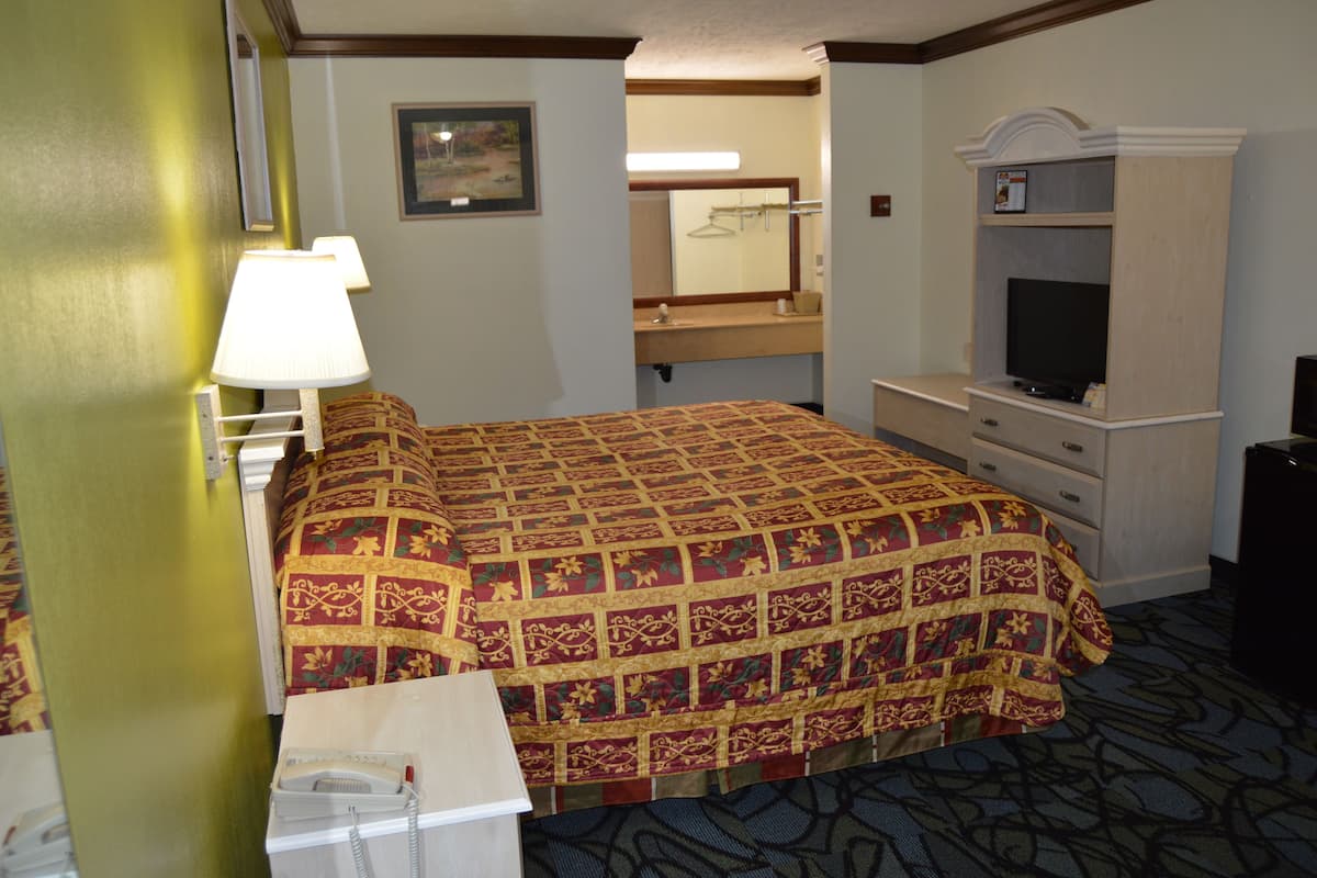 A hotel room with a bed, a desk with a telephone, a television, a mirror, and a dresser.
