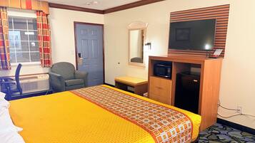 A hotel room with a bed, a desk, a chair, a television, and a microwave.