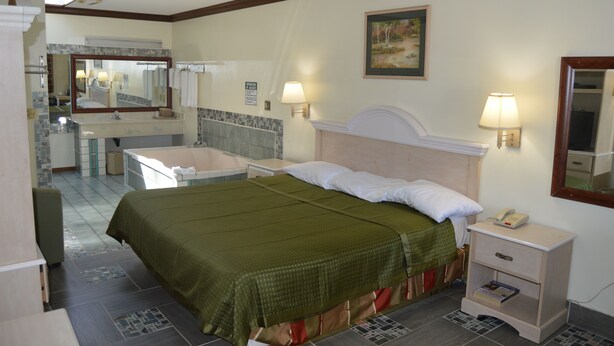 Une chambre d’hôtel comprenant un lit, une table de chevet, une commode et une salle de bain avec un lavabo et un miroir.