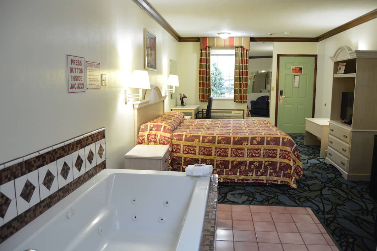 A hotel room with a bed, a desk, a chair, a bathroom with a bathtub, and a television.