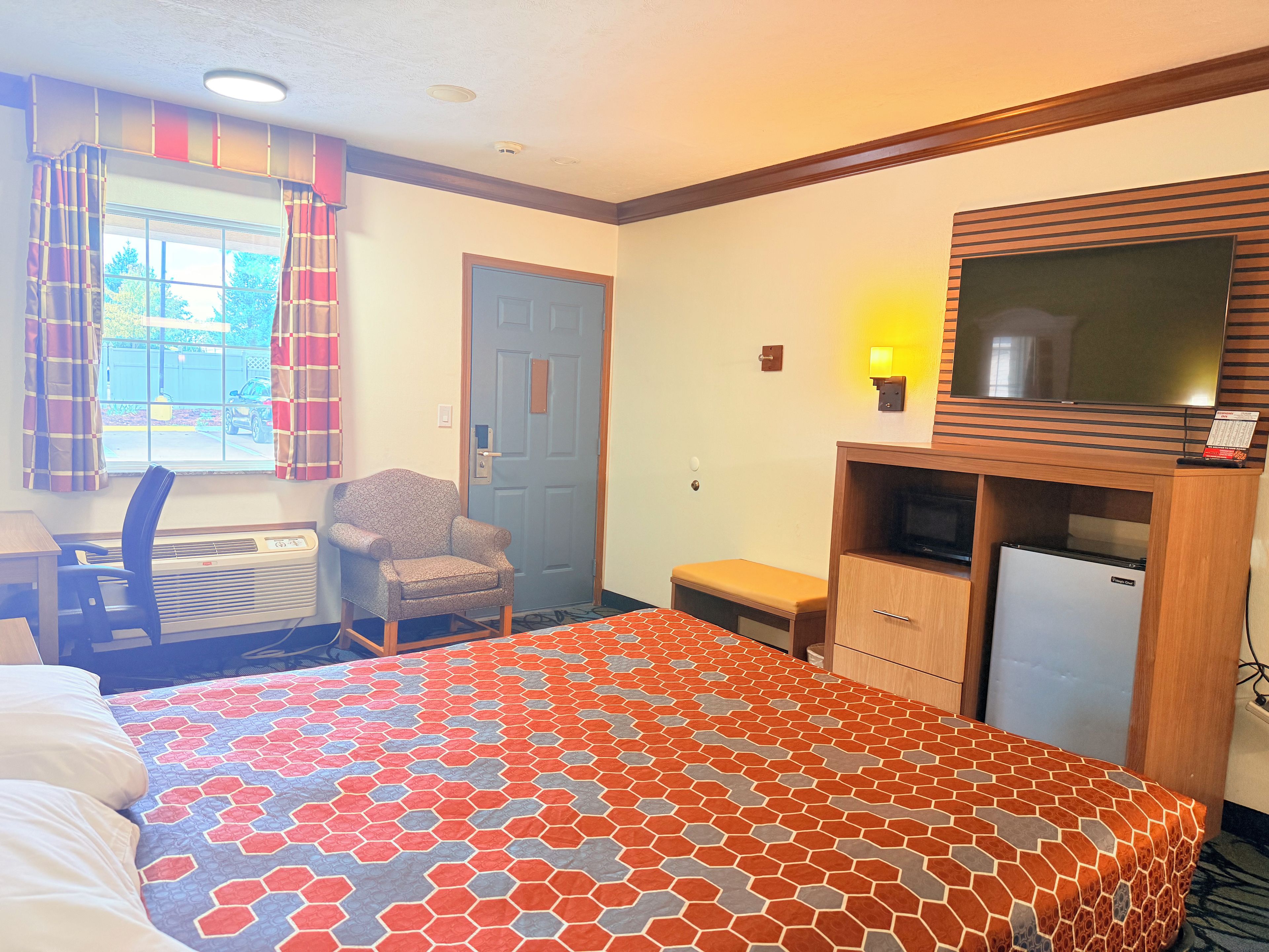 A hotel room with a bed, a desk, a chair, a television, and a small refrigerator.