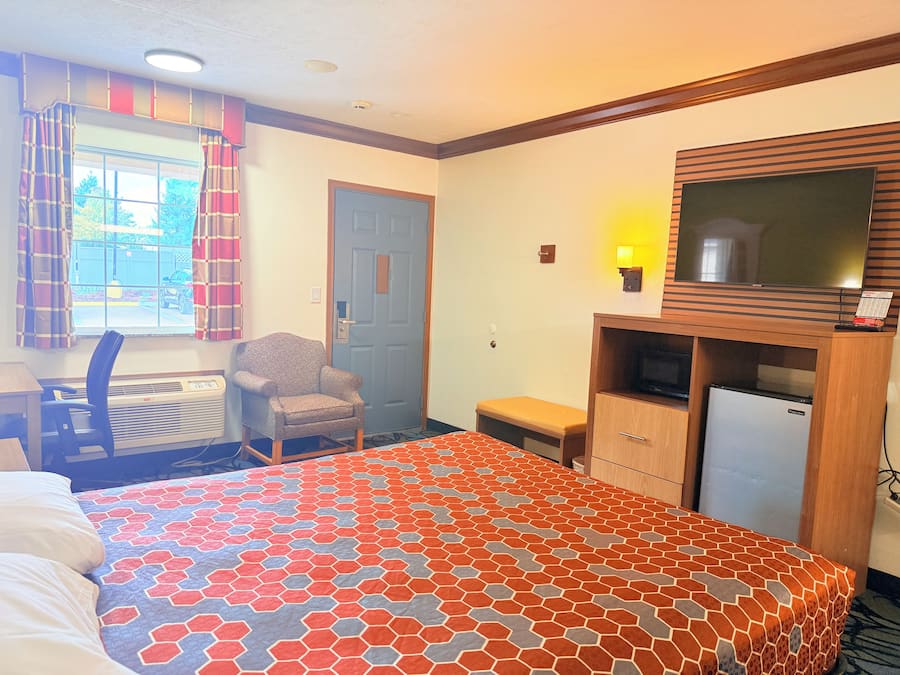 A hotel room with a bed, a desk, a chair, a television, and a small refrigerator.