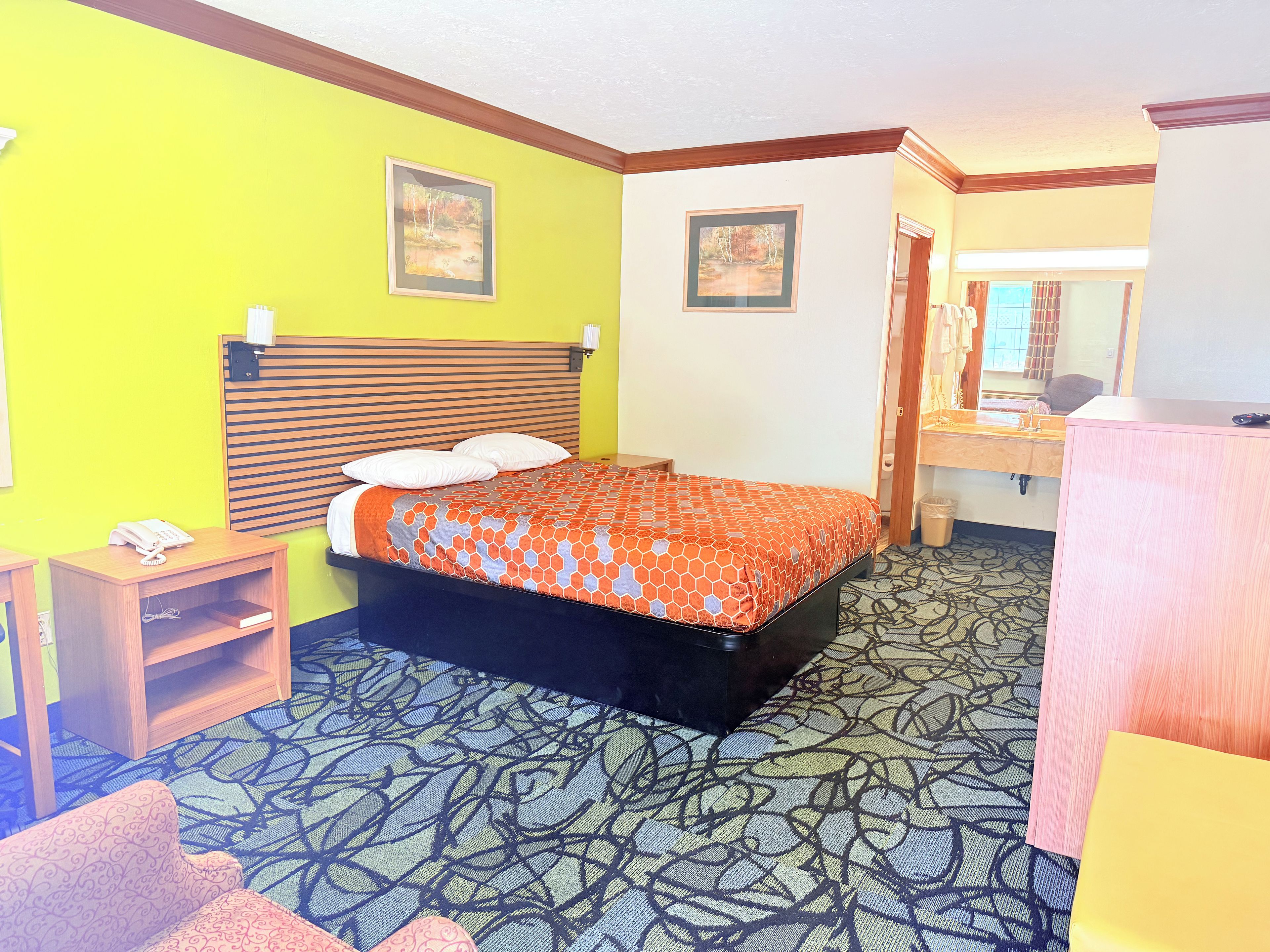 A hotel room with a bed, bedside table, and a desk with a chair.