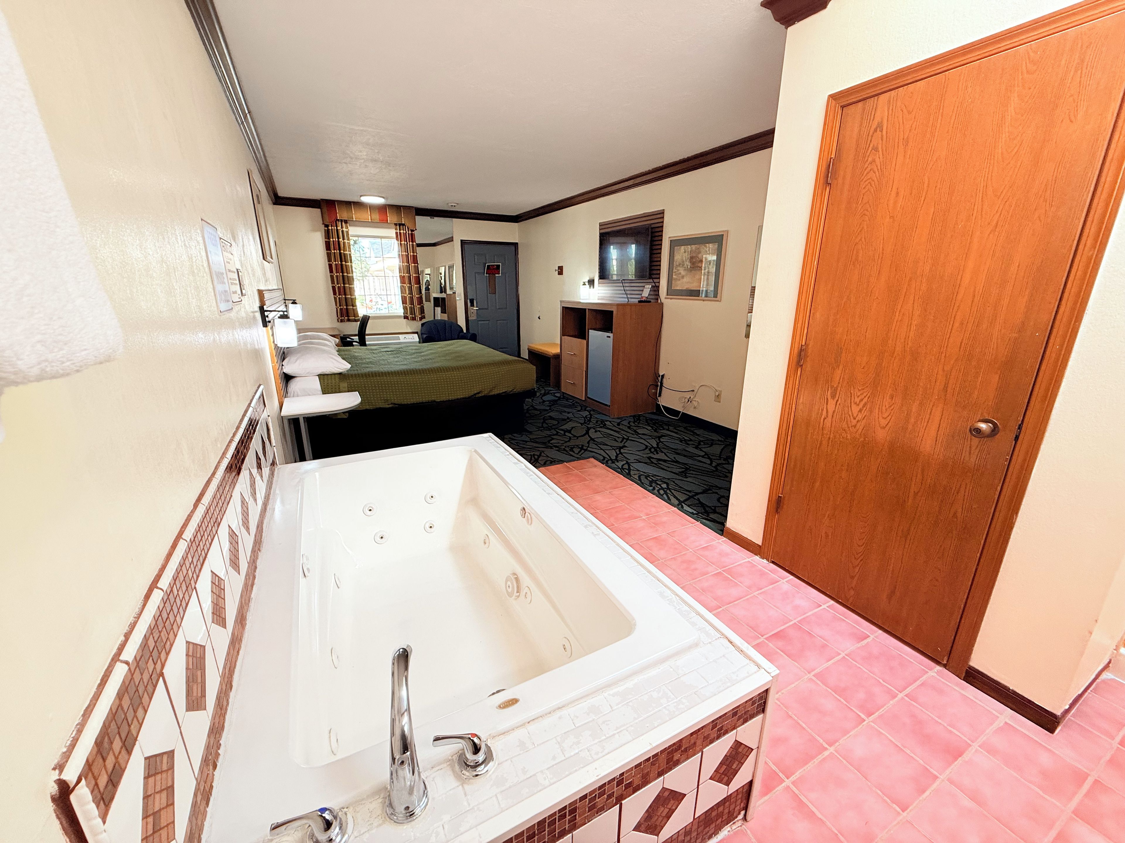 Habitación de hotel con una bañera grande, cama, escritorio y armario.
