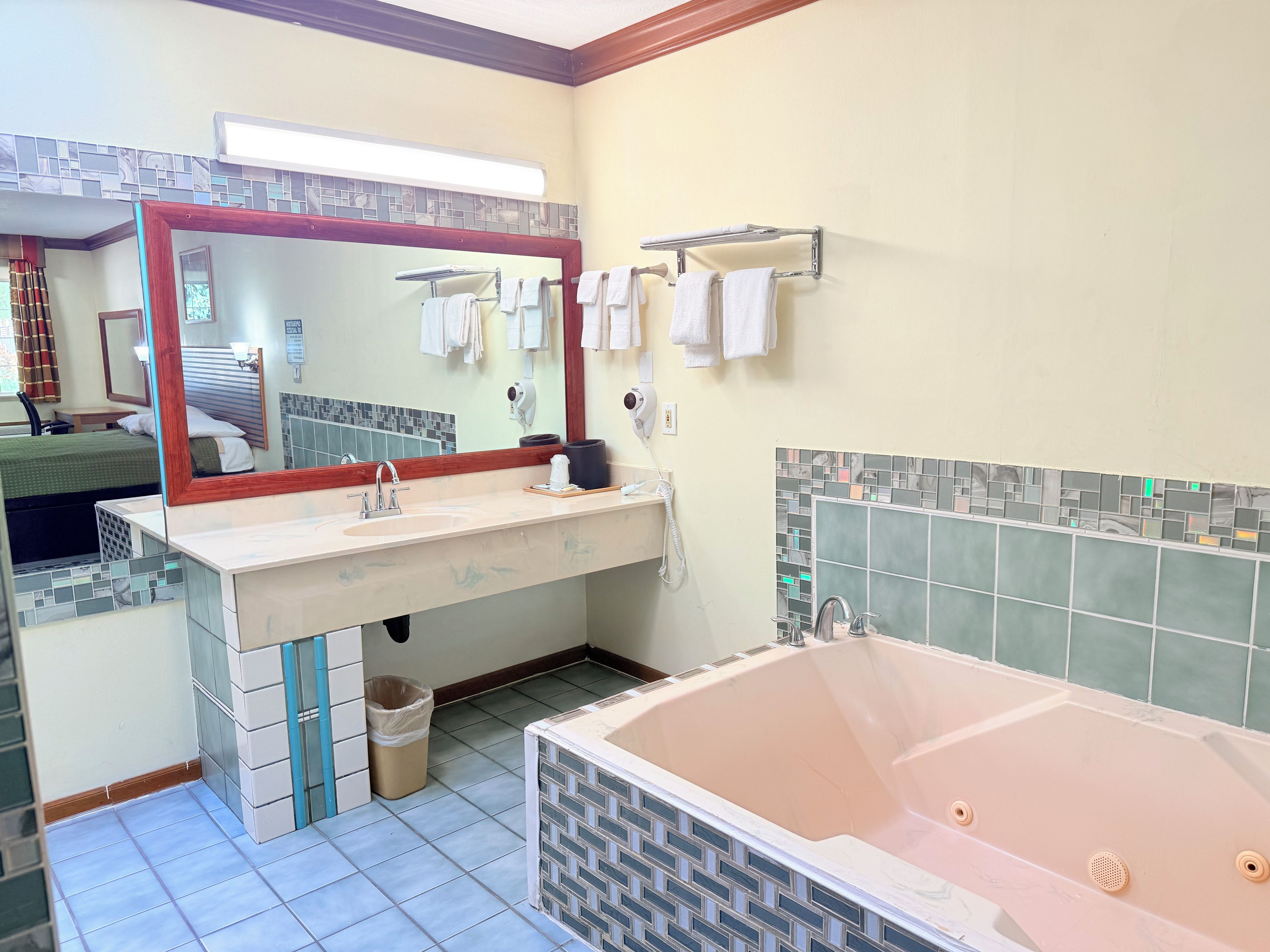 Un bagno con uno specchio grande, un lavandino, una vasca e un cestino.