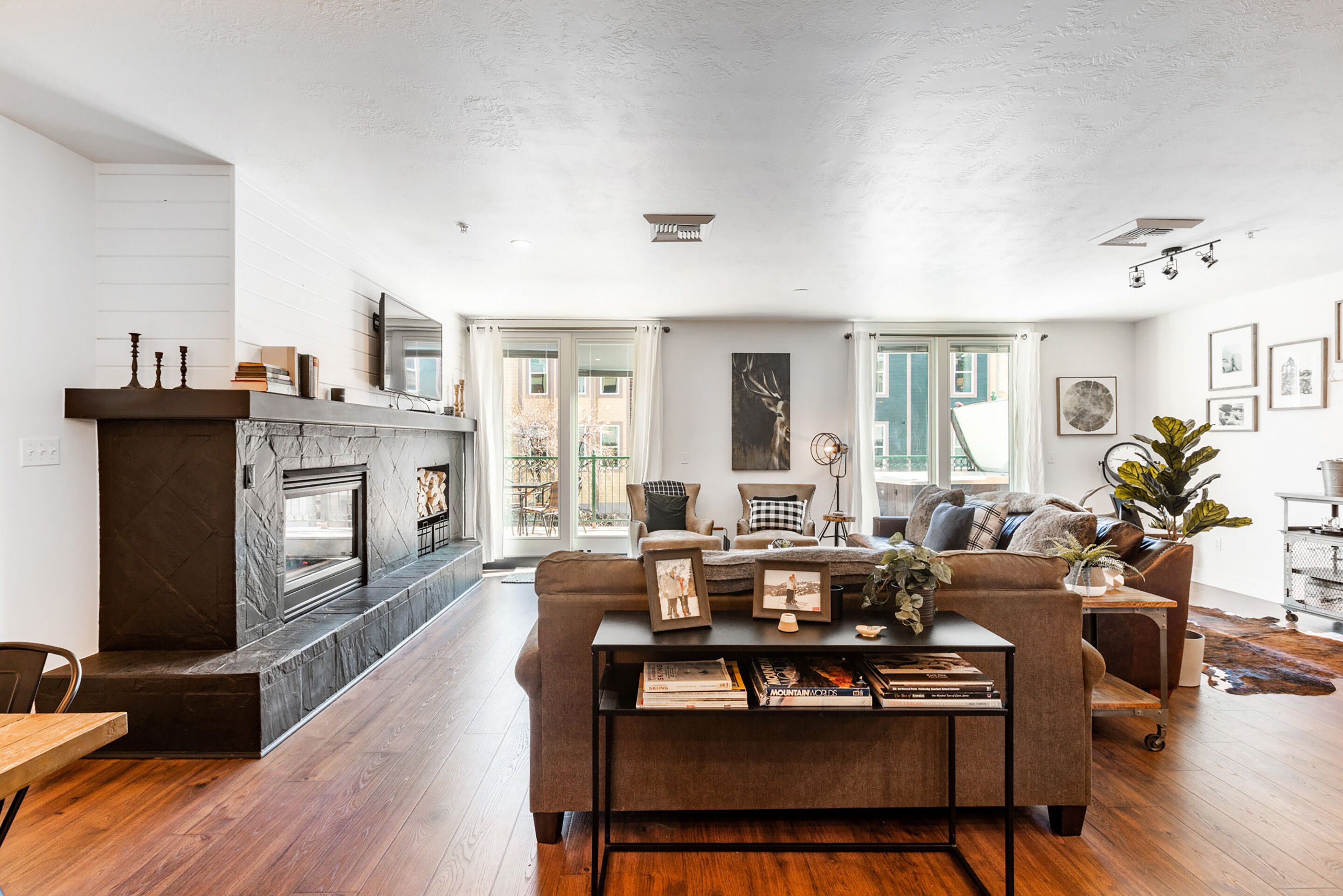 Een moderne woonkamer met een open haard, een bank, een bijzettafeltje met boeken en uitzicht op de omgeving.