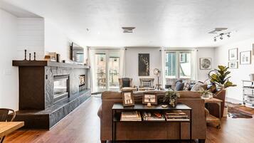 A modern living room with a fireplace, a sofa, a coffee table with books, and a view of the outdoors.
