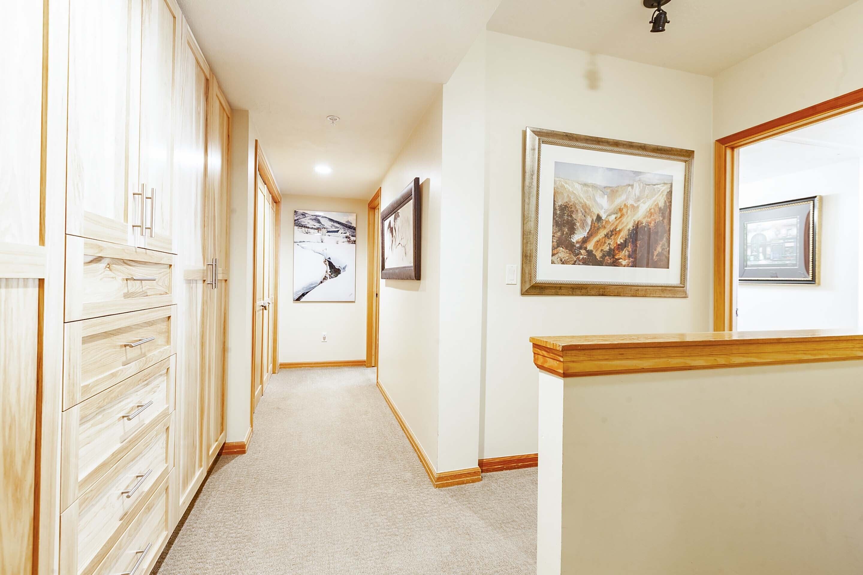 A hallway with wooden cabinets, framed artwork, and a carpeted floor.