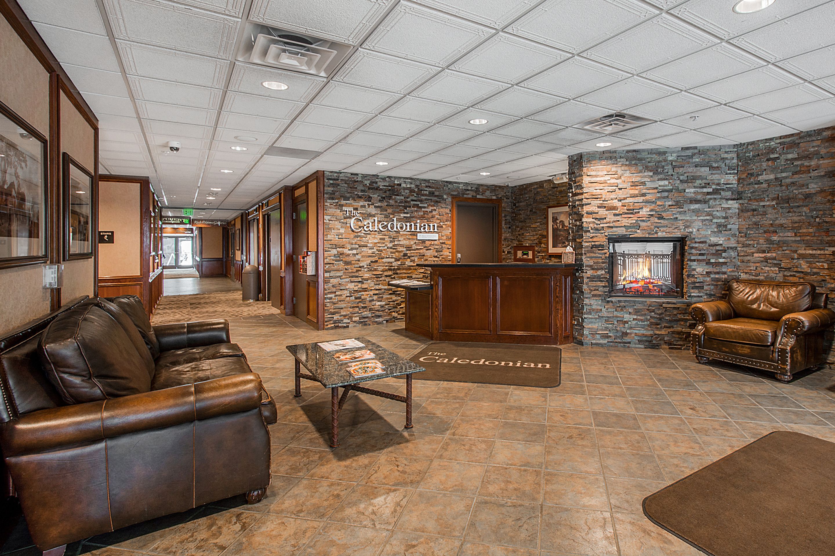 A lobby with a stone wall, leather sofas, a reception desk, and a fireplace.