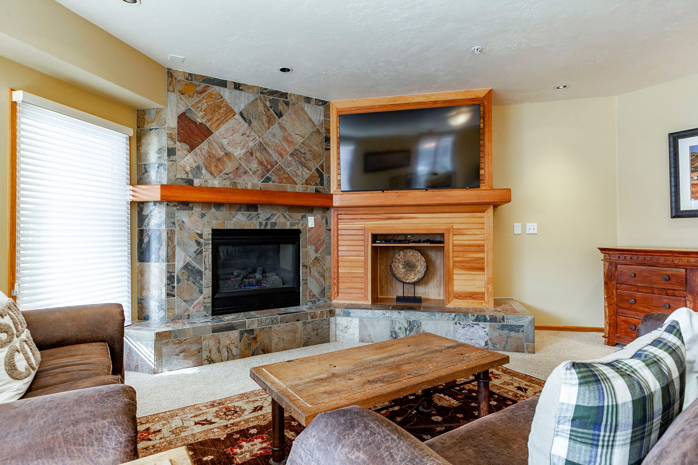 A living room with a stone fireplace, a flat-screen TV mounted above it, and a wooden cabinet below.