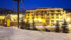 Een meerlaags hotel met een skilift op de achtergrond, omgeven door sneeuw en bomen.