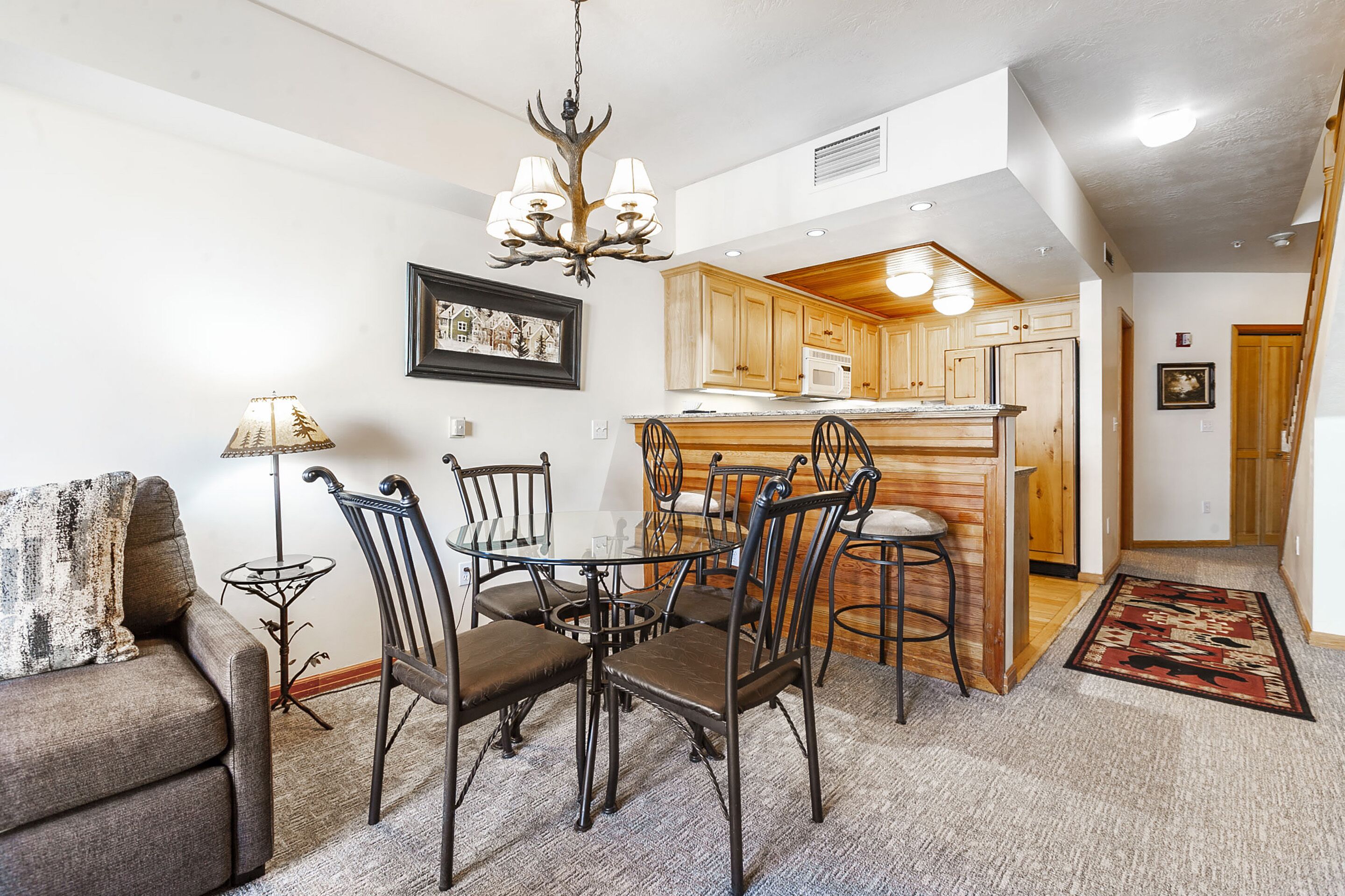 A dining area with a table and chairs, a chandelier, and a kitchen in the background.