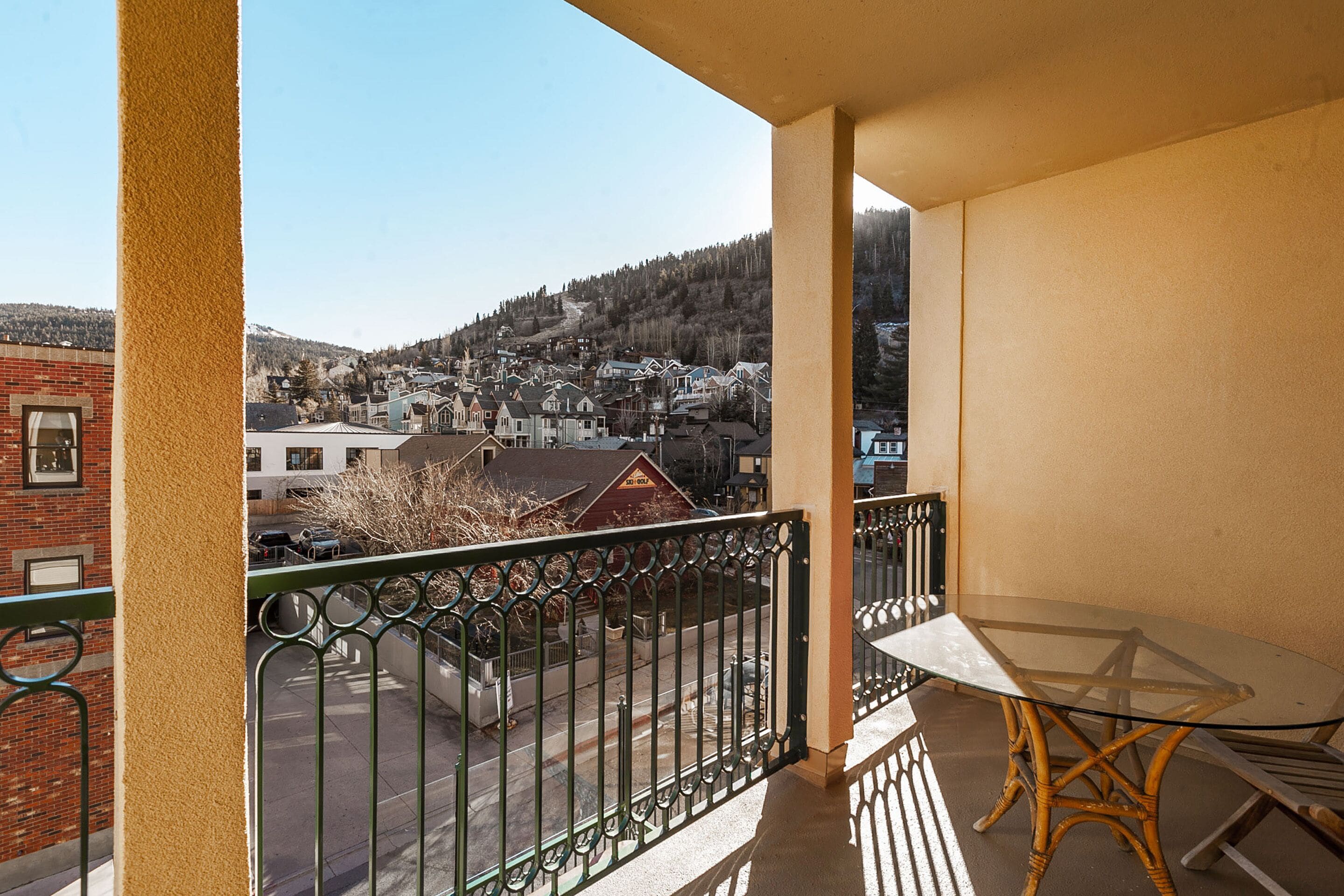Un balcone con un tavolo e sedie in vetro, affacciato su una zona residenziale con case e un paesaggio collinare.