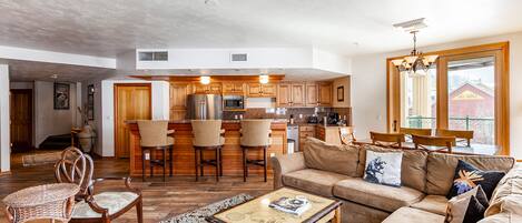 A spacious living area with a sofa, chairs, a coffee table, and a kitchen in the background.
