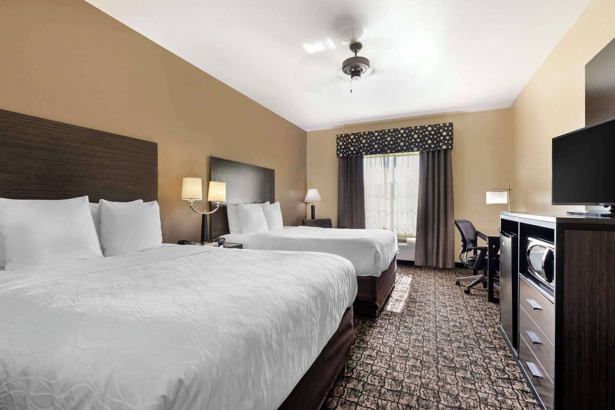 A hotel room with two beds, a desk, a TV, and a ceiling fan.