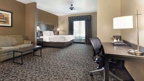 A hotel room with a bed, a desk, a chair, a sofa, a coffee table, and a lamp.