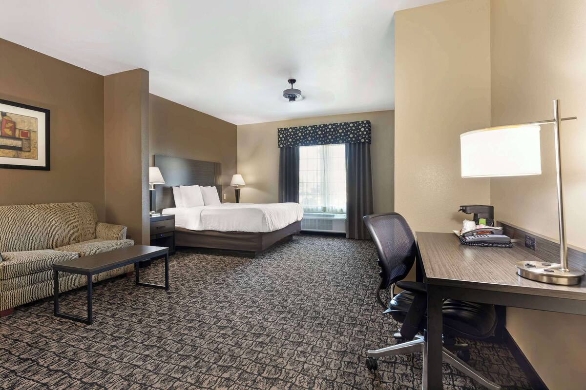 A hotel room with a bed, a desk, a chair, a sofa, a coffee table, and a lamp.