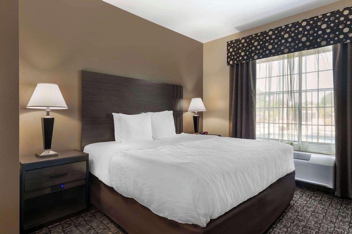 A hotel room with a large bed, two bedside lamps, a nightstand, and a window with curtains.