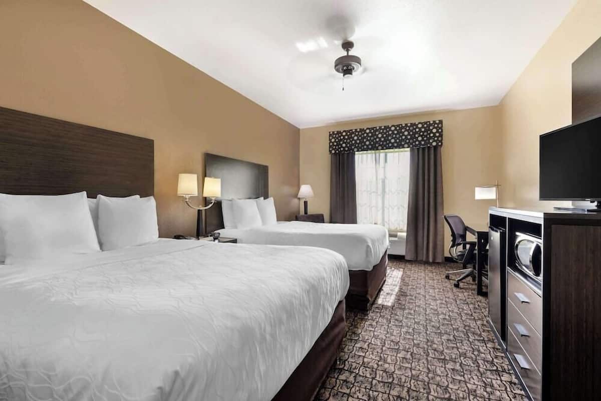 A hotel room with two beds, a desk, a television, and a ceiling fan.