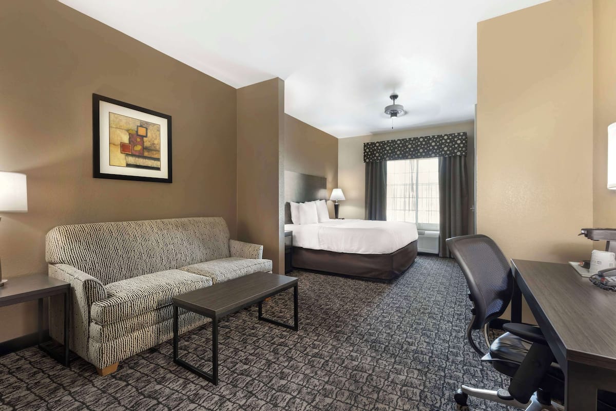 A hotel room with a sofa, a bed, a desk, and a framed picture on the wall.