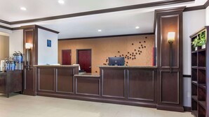 A reception area with a dark wood reception desk, a coffee station, and a wall-mounted TV.
