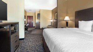 A hotel room with a bed, a desk with a computer, a chair, and a lamp.