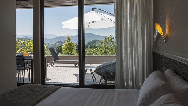 A hotel room with a bed, a view of the outdoors through a sliding door, and a patio area with a table, chairs, and an umbrella. -  FeelFree STAYS Basoa (San Sebastián)