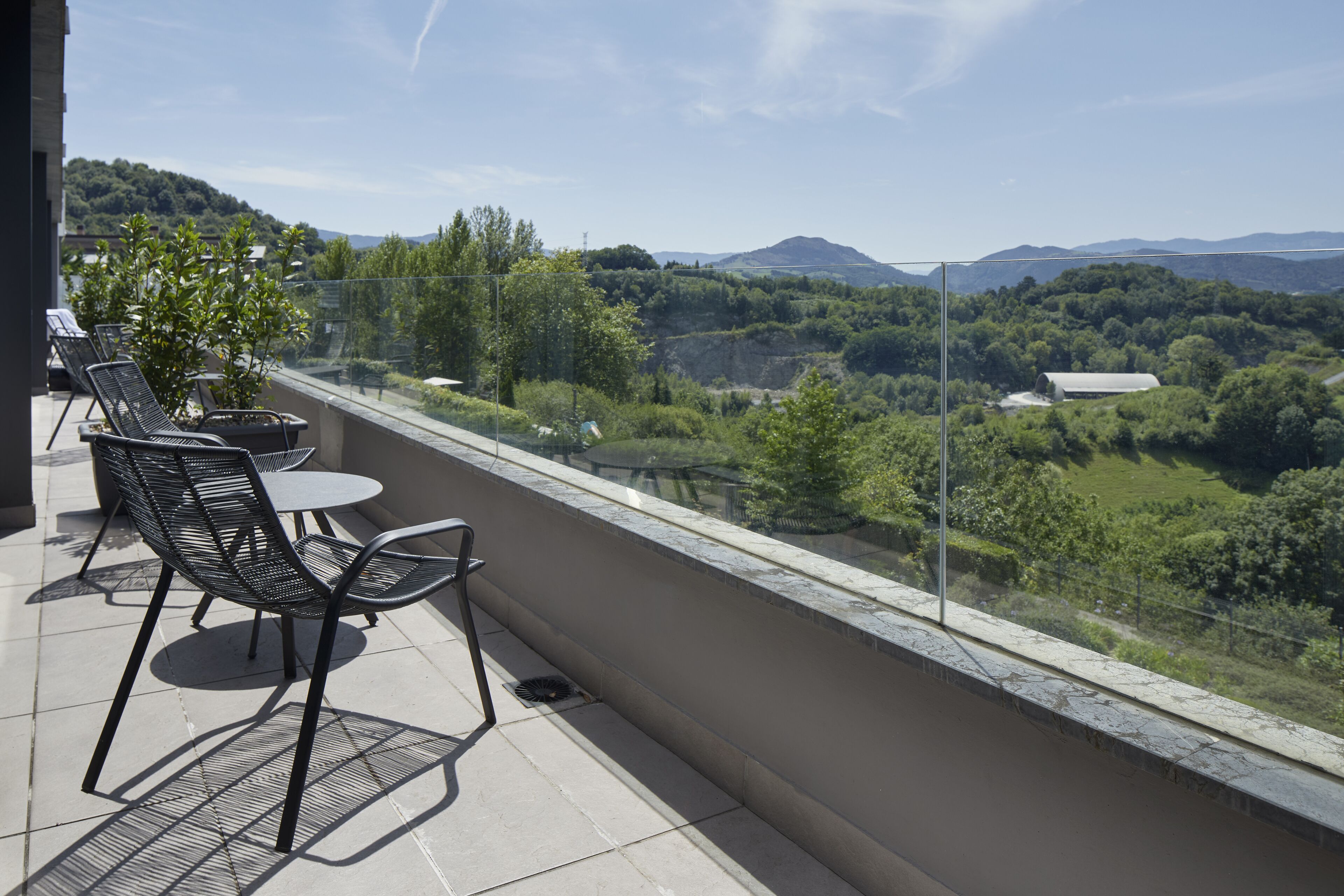 Un balcon avec une table et des chaises, donnant sur un paysage pittoresque, avec des arbres et des collines.