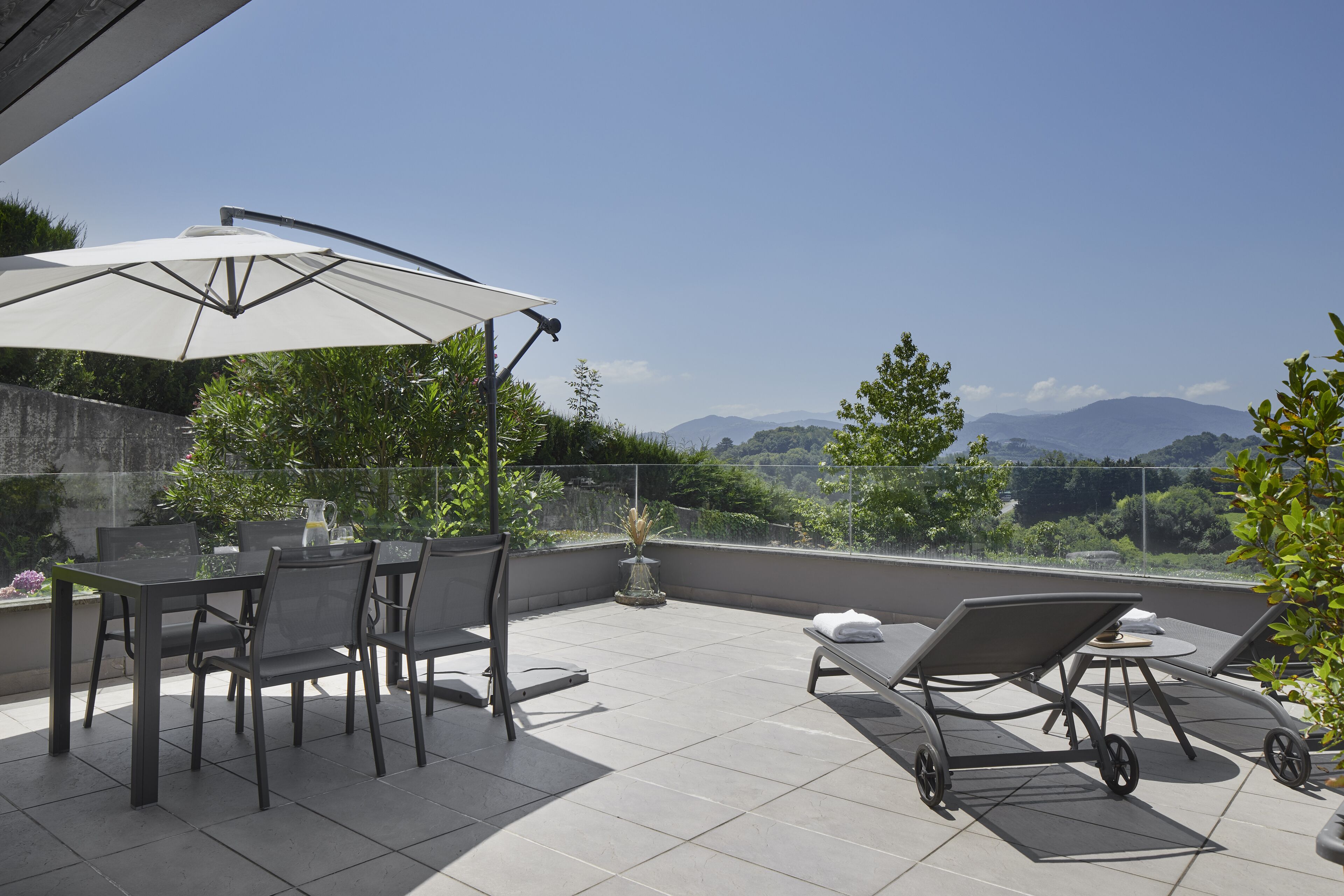 A terrace with a table and chairs, a sun lounger, and a large umbrella.