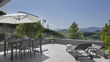 A terrace with a table and chairs, a sun lounger, and a large umbrella.