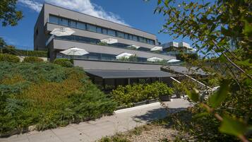 A modern building with multiple balconies, outdoor seating areas with umbrellas, and a landscaped garden.