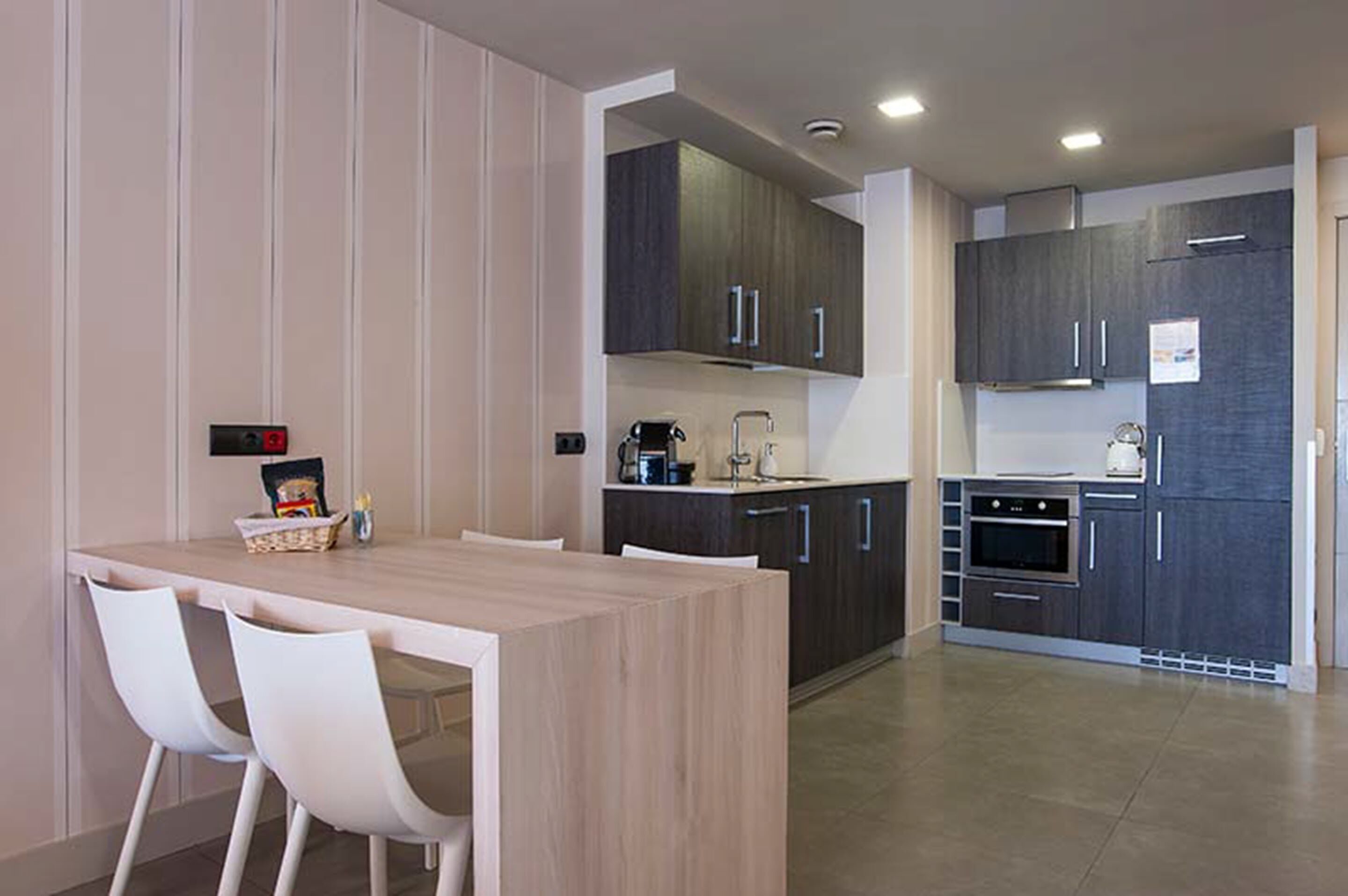 Una cocina moderna con armarios oscuros, una mesa de comedor de madera y sillas blancas.