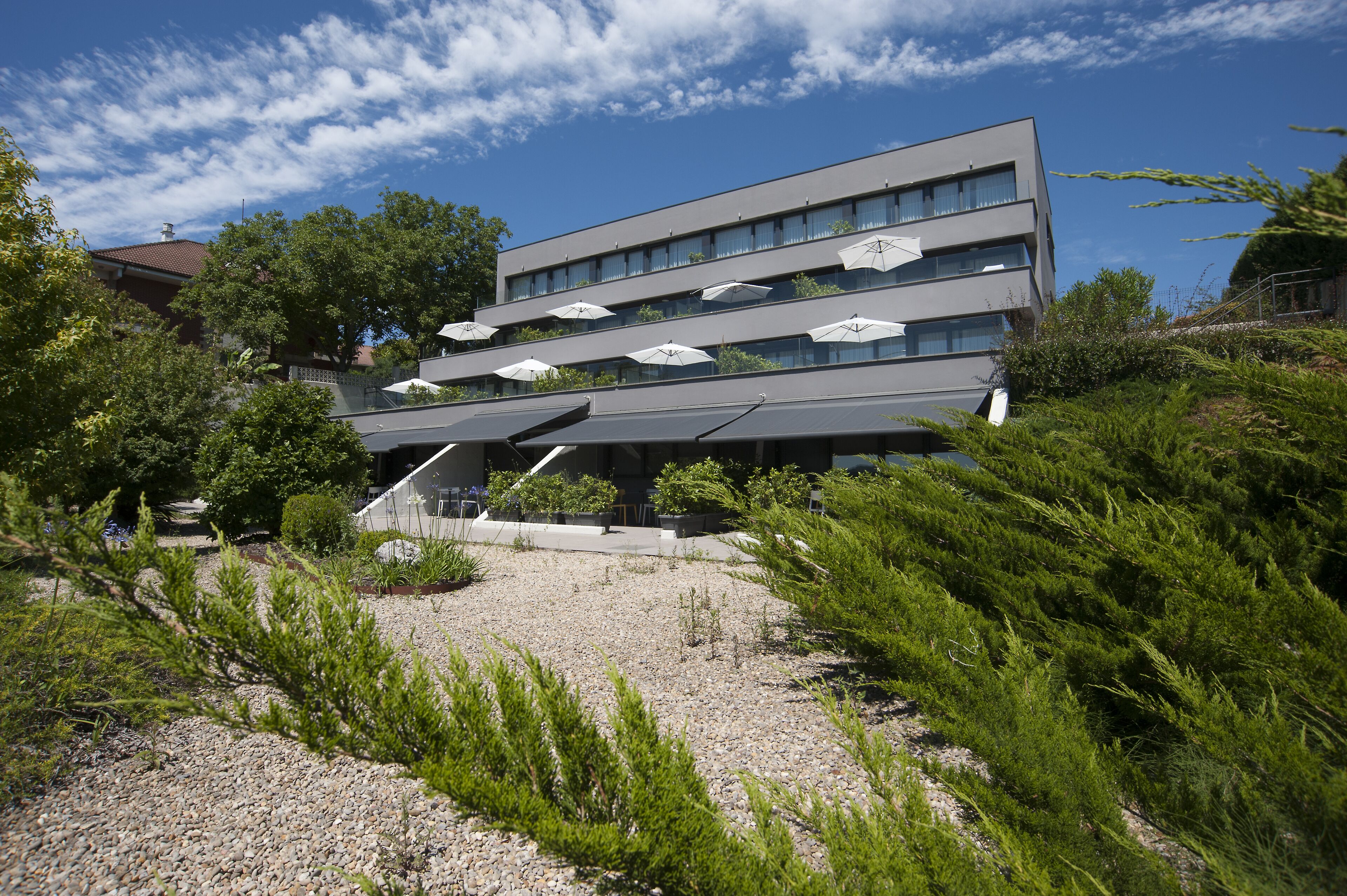 A modern building with multiple floors, outdoor umbrellas, and a gravel pathway.