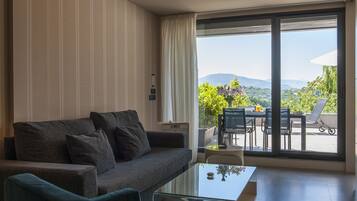 Een moderne woonkamer met een bank, een glazen salontafel en uitzicht op een balkon met buitenmeubilair.