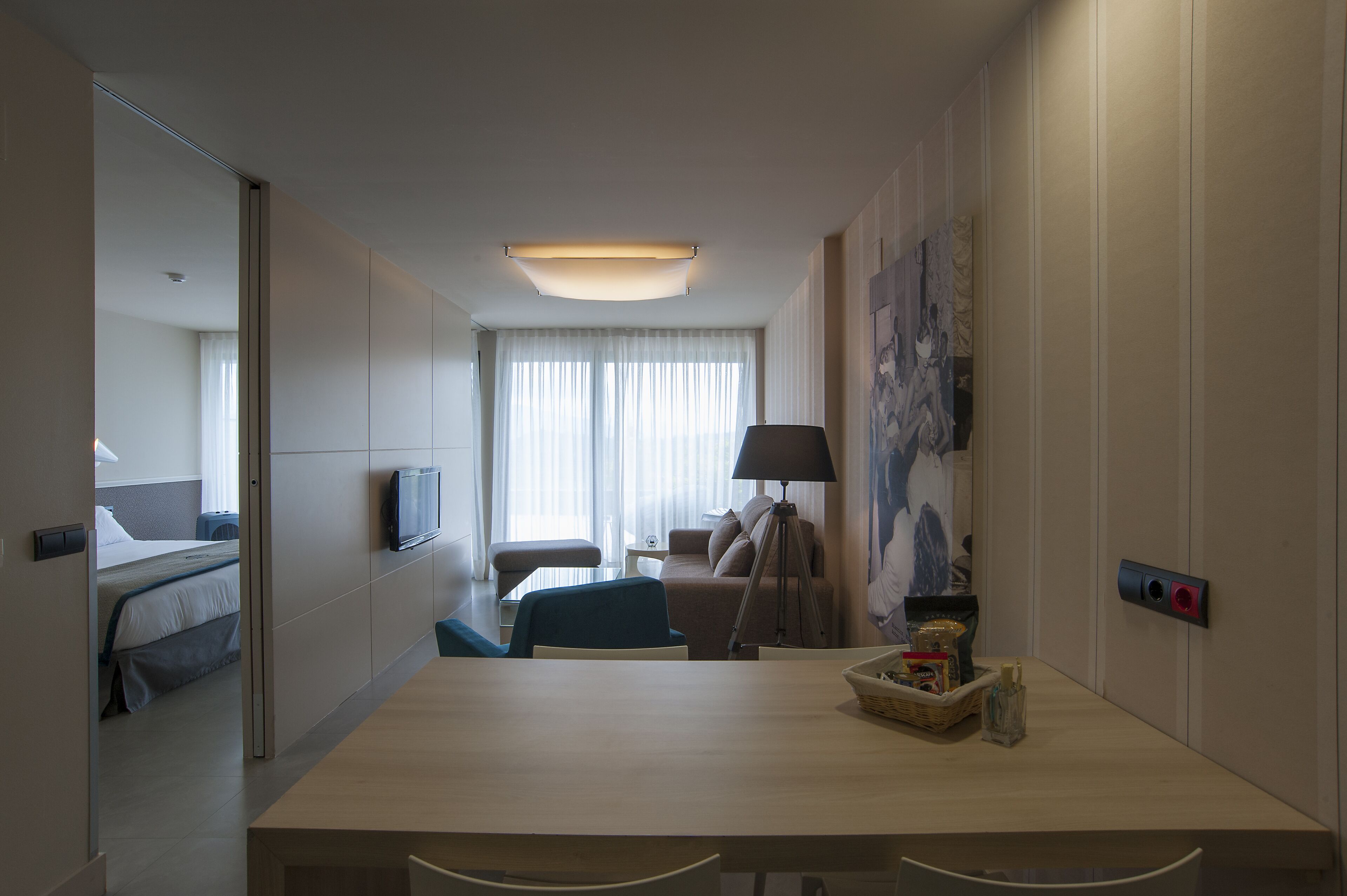 A hotel room with a bed, a desk, a chair, a lamp, a television, and a window with curtains.