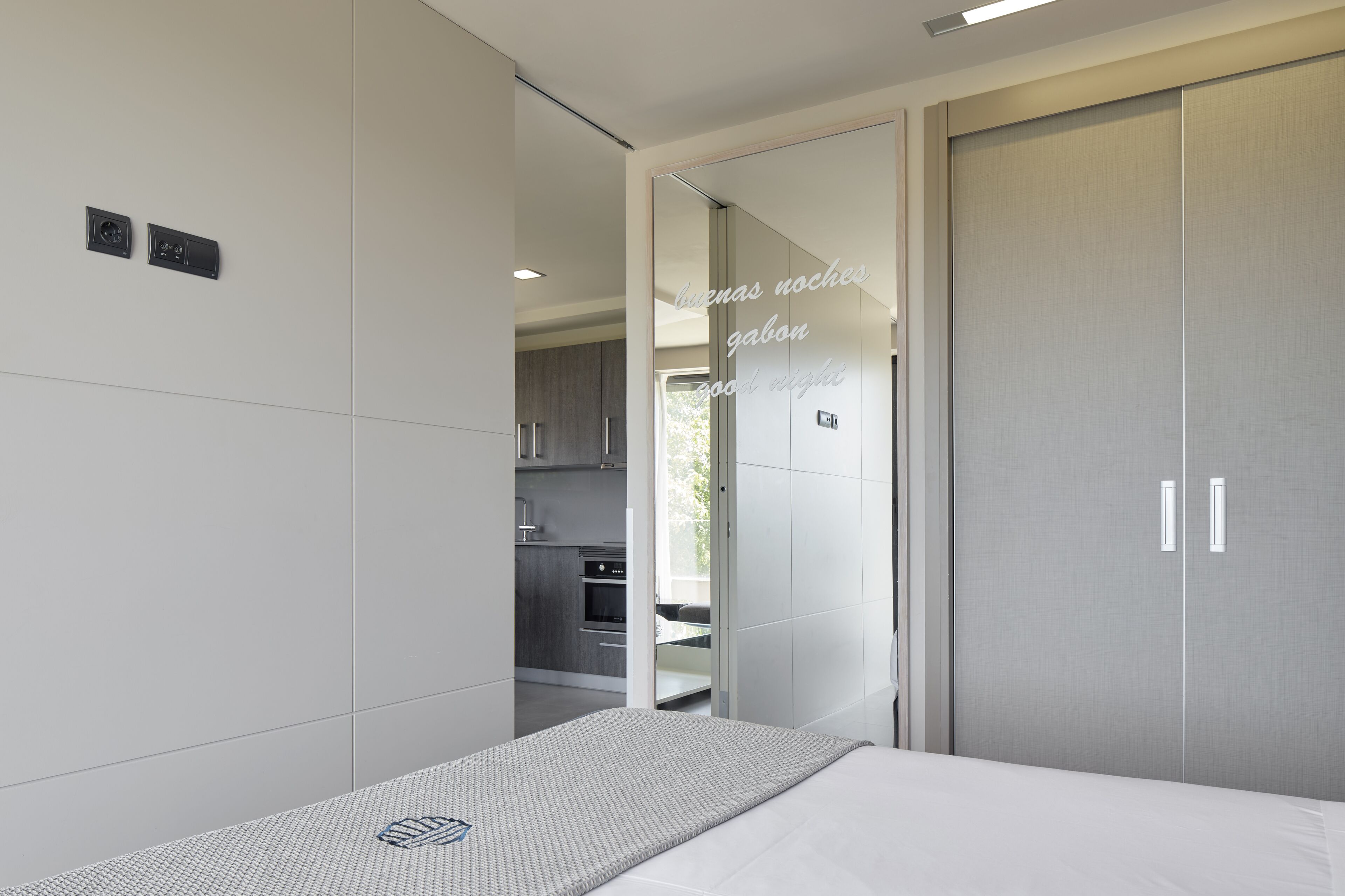 Ein modernes Schlafzimmer mit Bett, Kleiderschrank und Blick in die Küche.