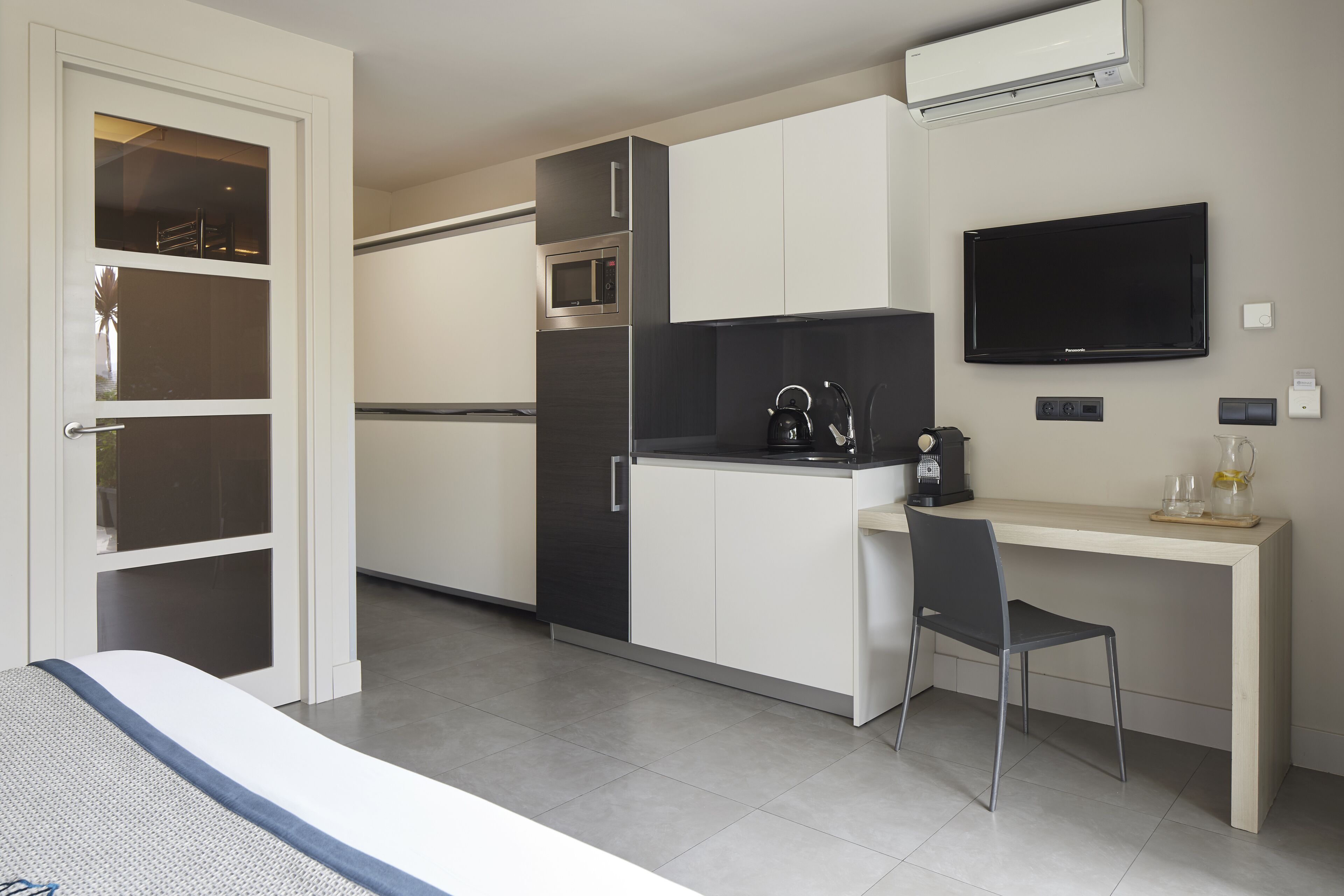 Una cucina moderna con forno a microonde, piano cottura e televisore a schermo piatto. C'è un'area pranzo con una sedia e un tavolo.
