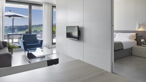 A modern hotel room with a large window, a flat-screen TV, a sofa, a coffee table, and a bed with a nightstand. -  FeelFree STAYS Basoa (San Sebastián)